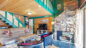 A cozy living room with a stone fireplace, wooden ceiling, and a television. - Cabin with Eight SHARC Passes, Access to Shared Pools, Hot Tub & Other Amenities (Sunriver)