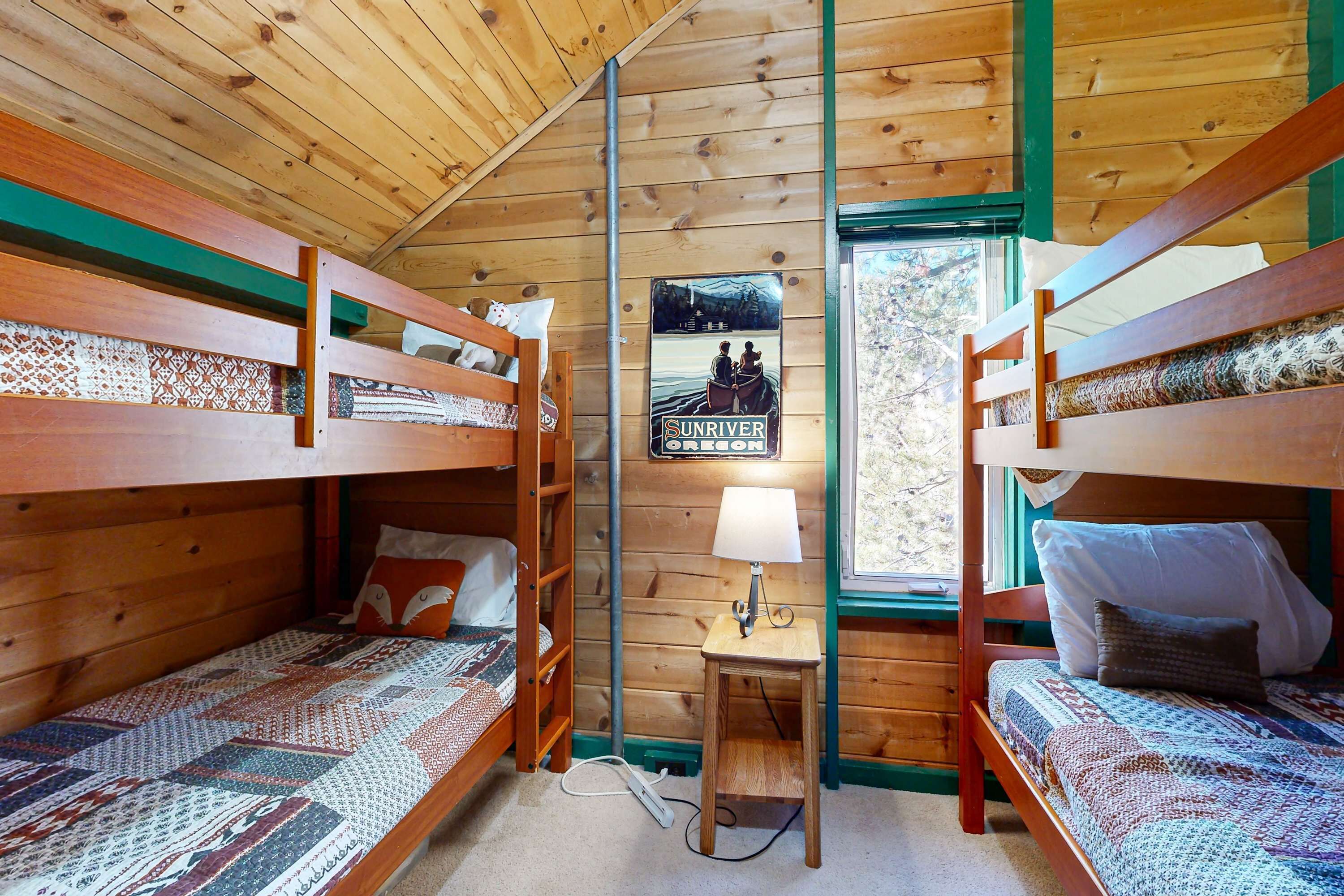 A cabin with two bunk beds, a small table with a lamp, and a poster on the wall.