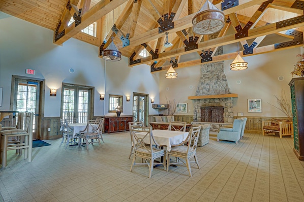 A spacious interior with wooden beams, a stone fireplace, and a dining area with tables and chairs.