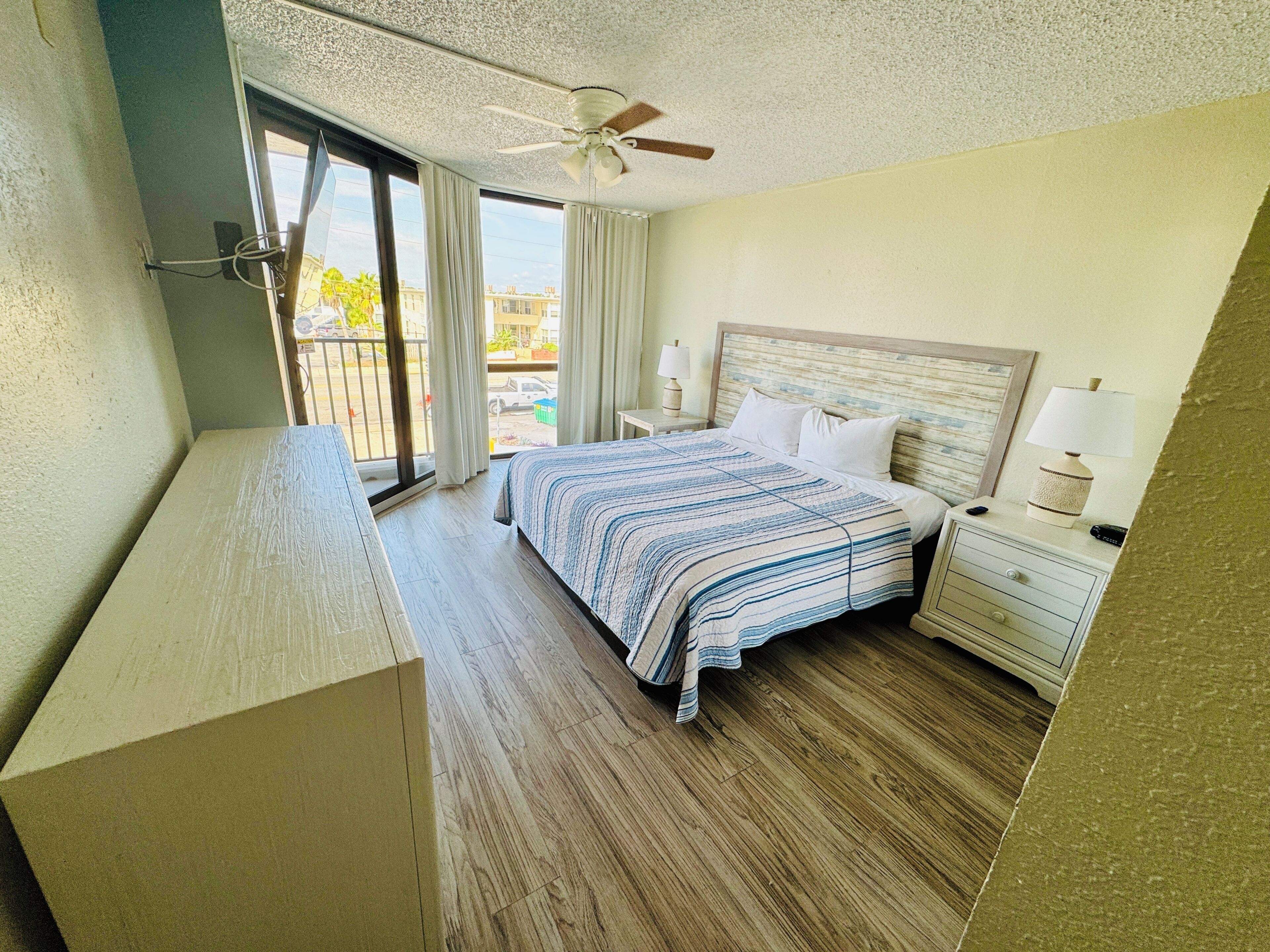 A hotel room with a bed, bedside tables, a ceiling fan, and a view of the outside.