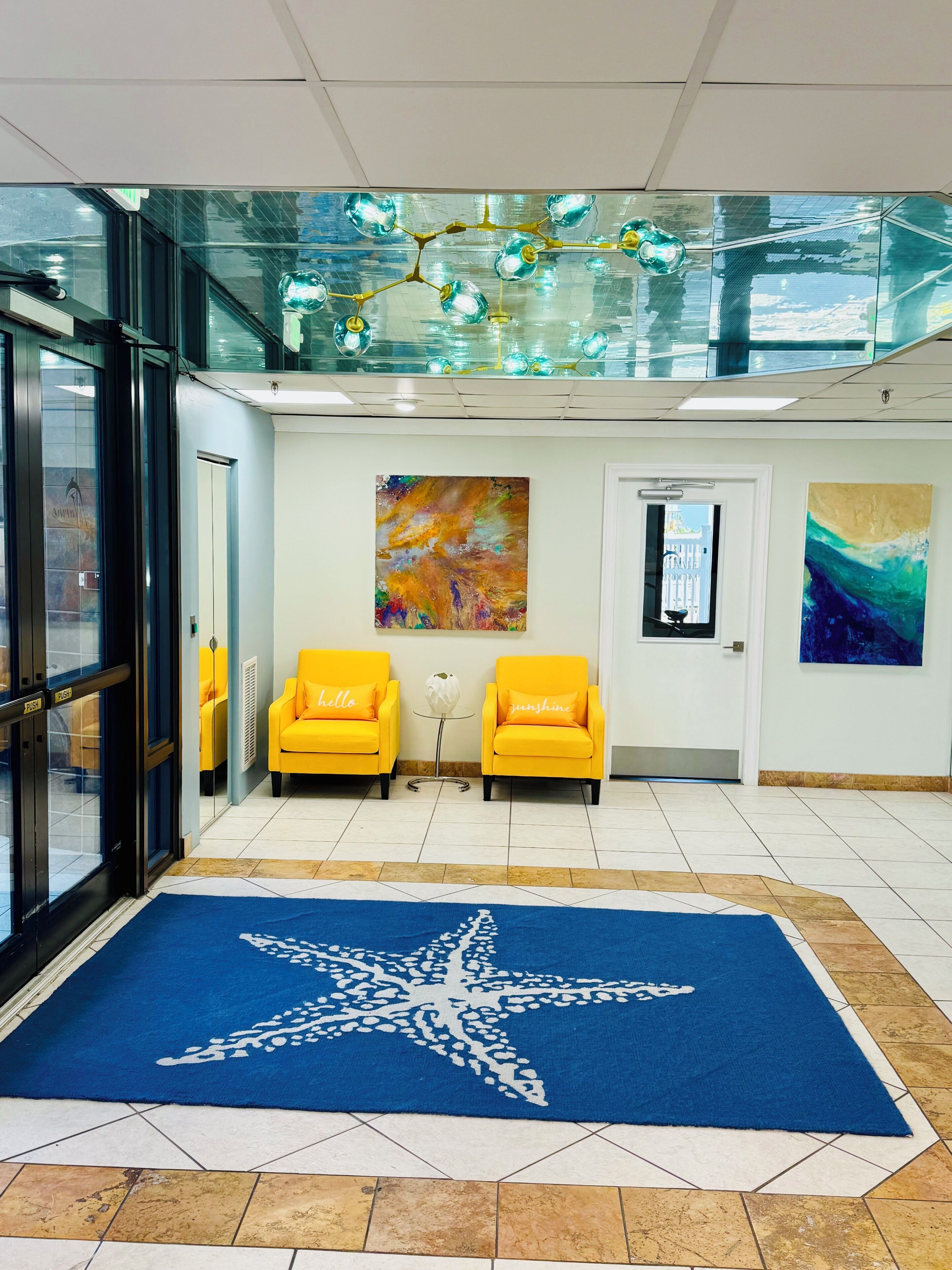 A lobby with two yellow armchairs, a blue star-patterned carpet, and abstract paintings on the walls.