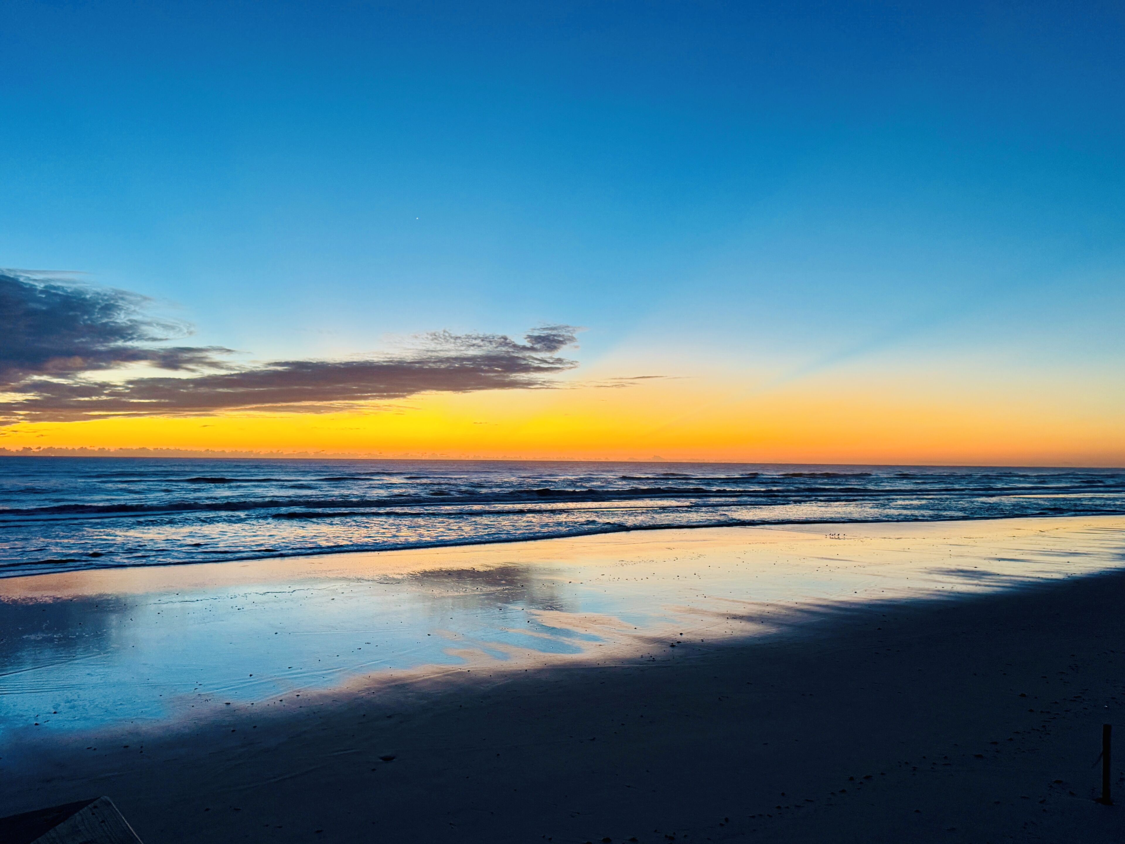A beach with a sunset, calm waves, and a clear sky.