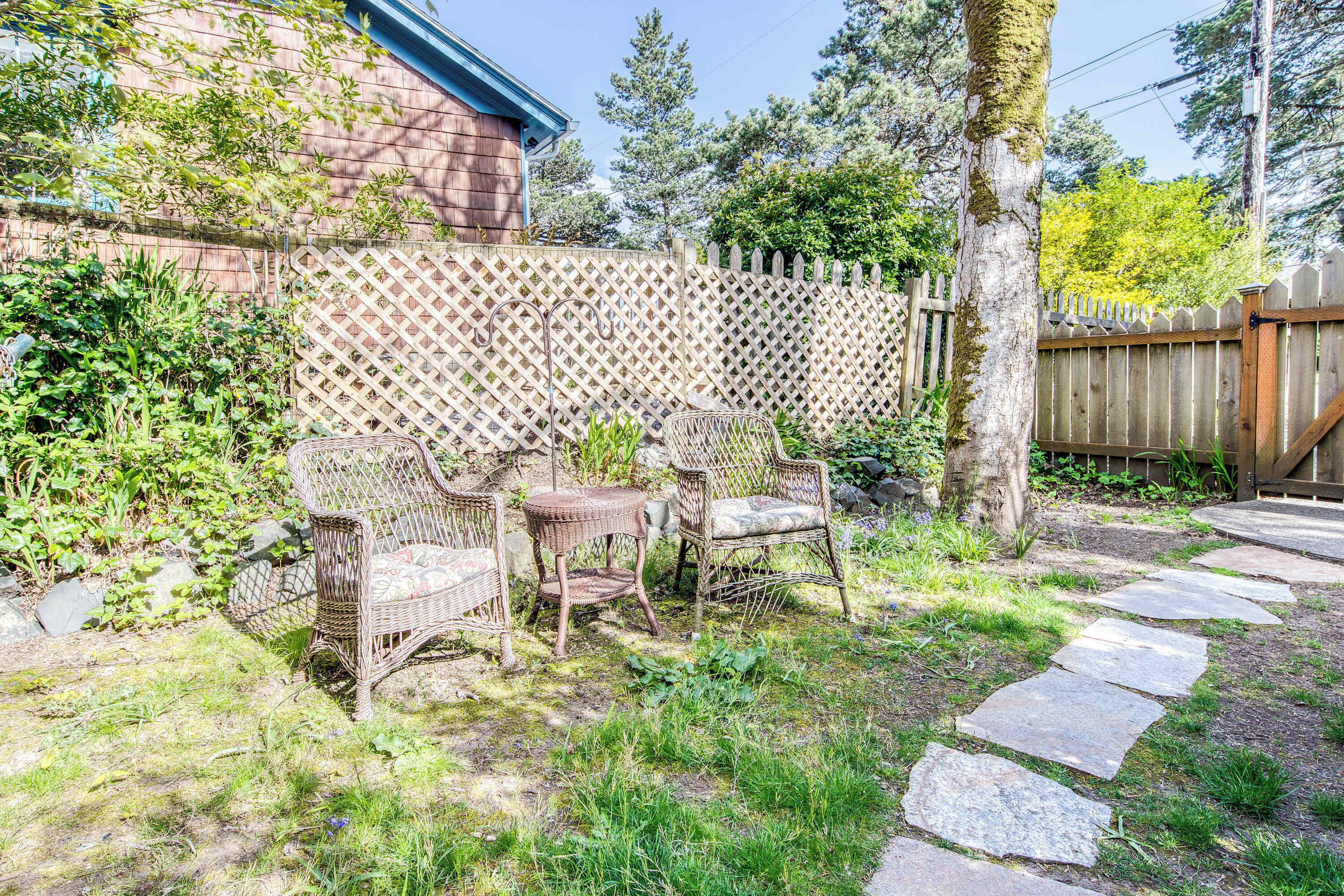 Un jardin avec une clôture en bois, un chemin de pierres et des meubles en osier.