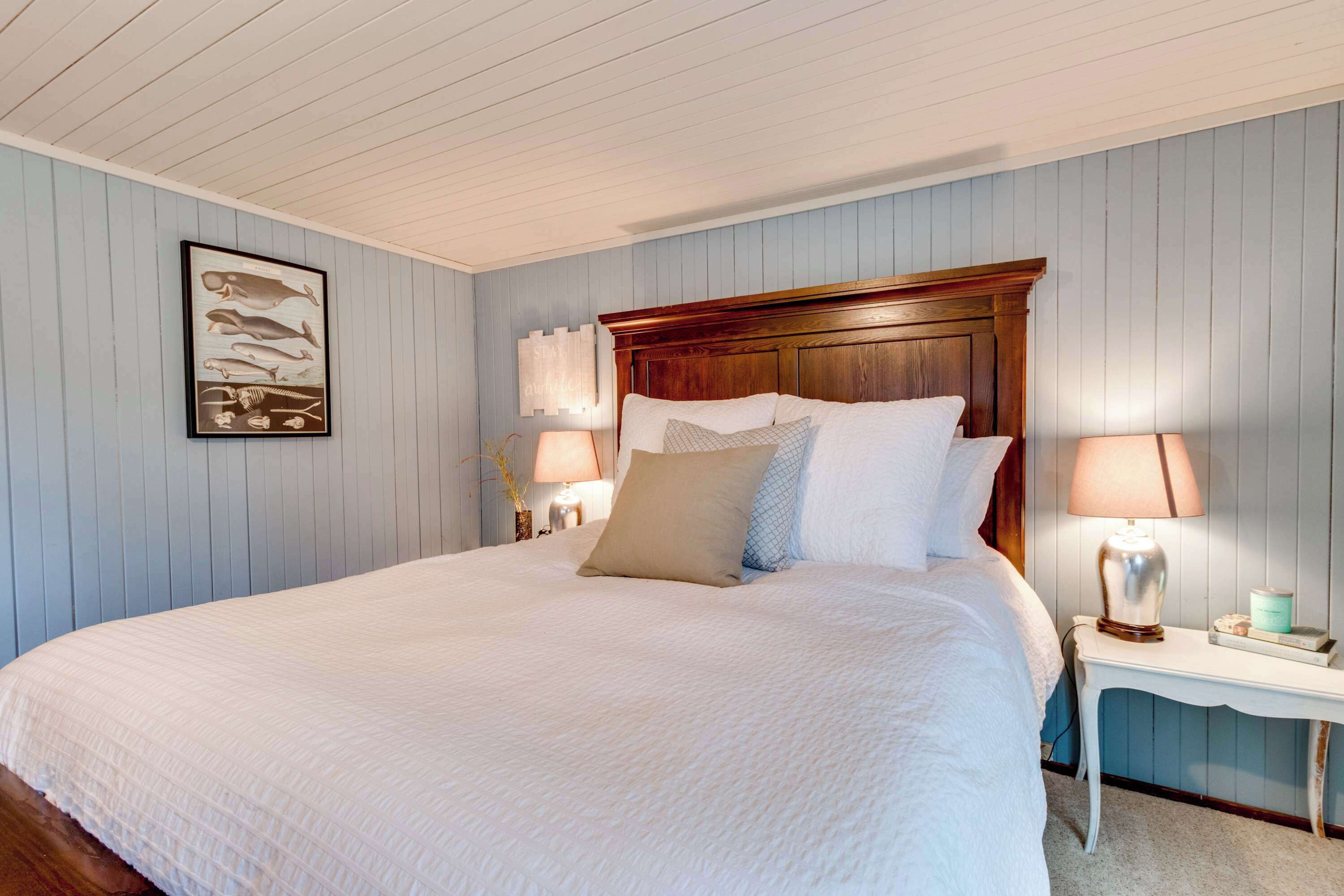 A bedroom with a large bed, wooden headboard, two bedside tables with lamps, and a wall-mounted artwork.