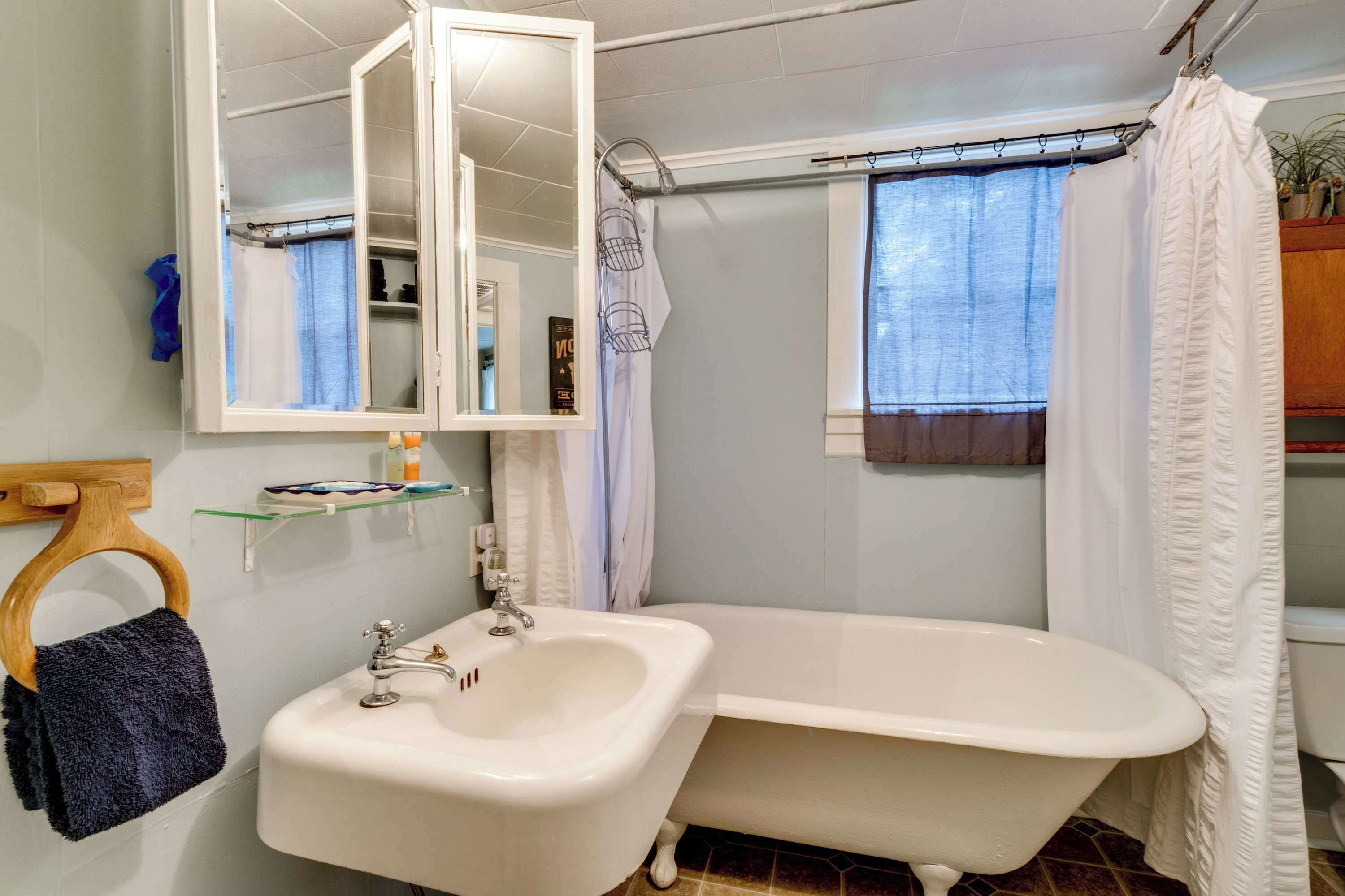 A bathroom with a white bathtub, a sink, a mirror, and a shower curtain.