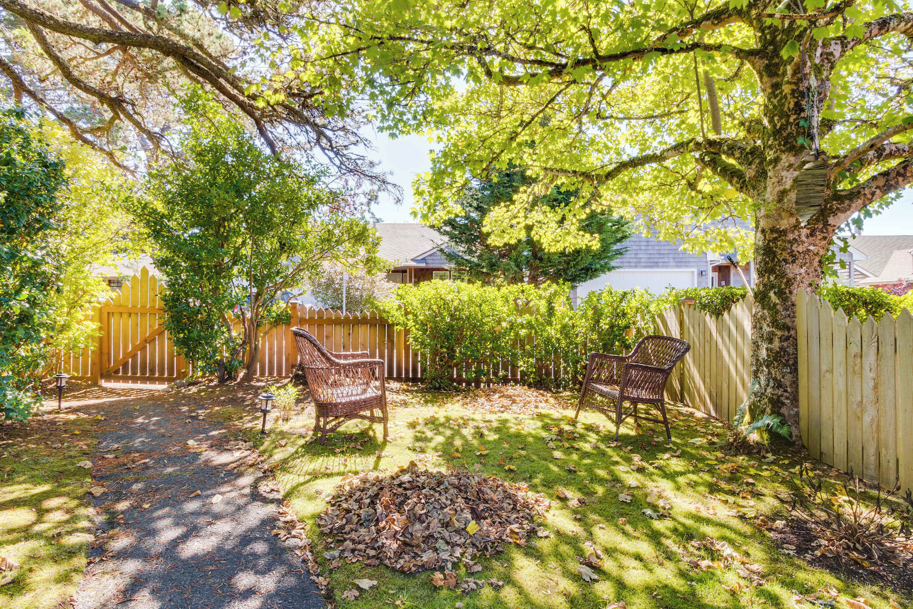 A backyard with a wooden fence, two wicker chairs, and a pile of leaves.