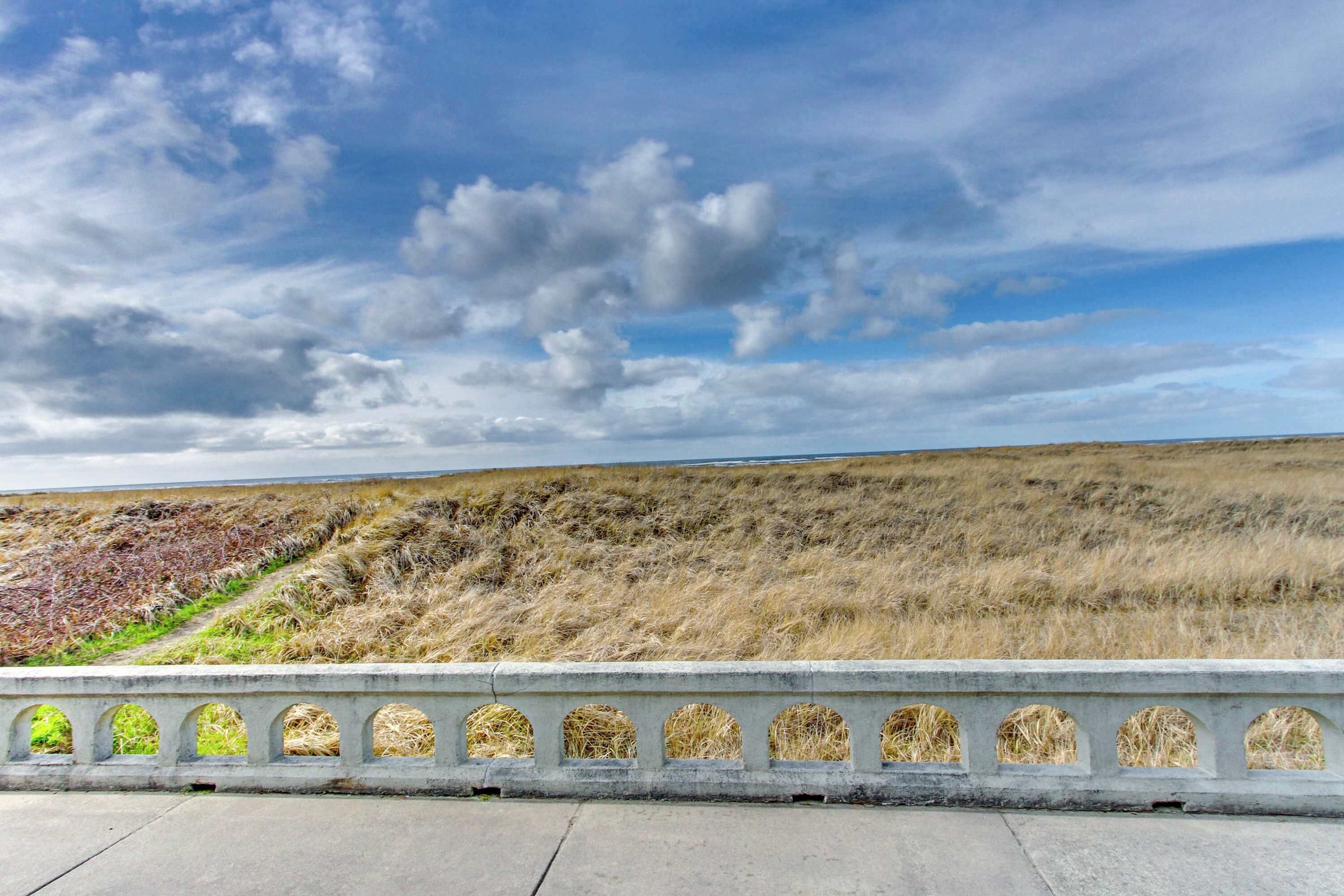Een betonnen barrière met boogvormige openingen, een grasveld en een bewolkte lucht.