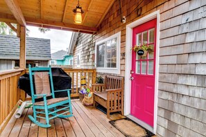 A wooden deck with a rocking chair, a grill, and a bright pink door.