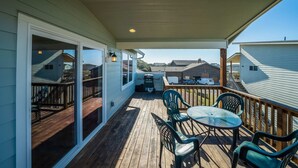 A covered deck with a table and chairs, a sliding glass door, and a view of neighboring houses. - Coastal cottage with stunning ocean views & private gas grill - dogs welcome (Gold Beach)