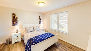 A bedroom with a bed, nightstands, a window, and a ceiling light. - Coastal cottage with stunning ocean views & private gas grill - dogs welcome (Gold Beach)