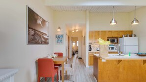 Una cocina moderna con armarios de madera, una isla central, iluminación colgante y un comedor con mesa y sillas.