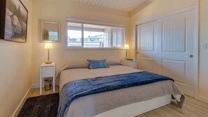 Un dormitorio con una cama, dos lámparas de noche, una ventana, una puerta y un cuadro en la pared.