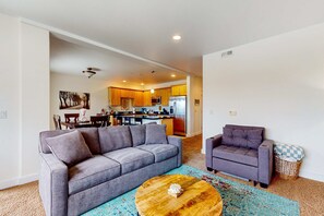 A living room with a grey sofa, a smaller grey armchair, a wooden coffee table, and a patterned rug.