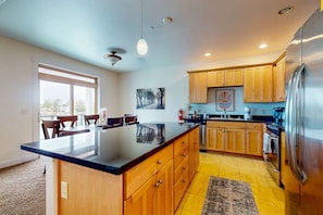 A modern kitchen with wooden cabinets, a large island, stainless steel appliances, and a dining area with chairs.