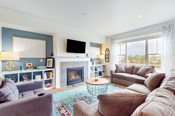 A living room with a fireplace, sofas, a TV, and a large window.