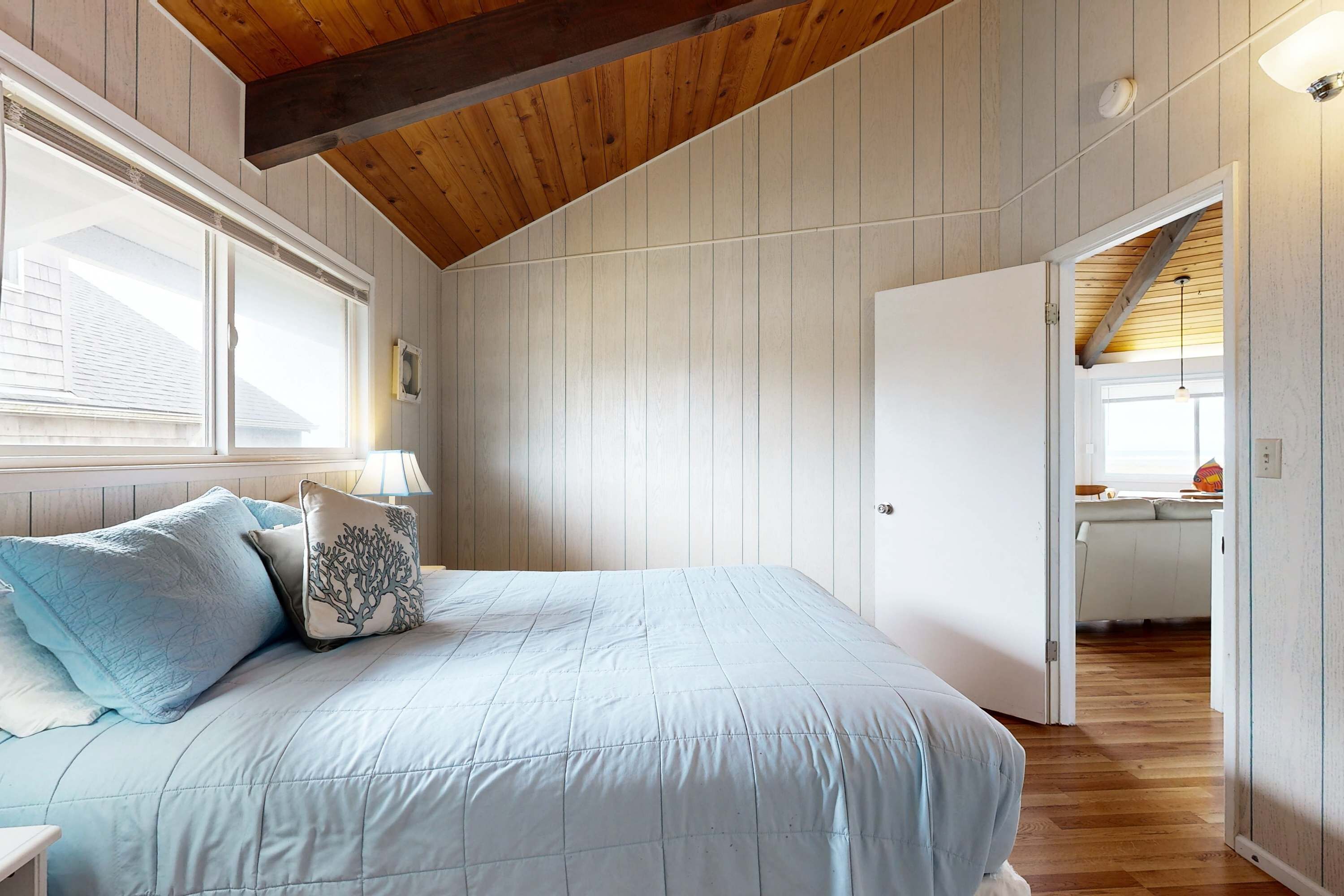A bedroom with a bed, a nightstand, a lamp, and a door leading to a kitchen.
