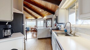 Una cocina moderna con armarios blancos, techo de madera y un ventanal amplio.