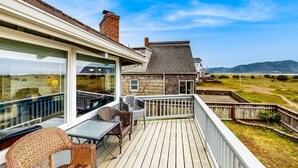 Una terraza de madera con mobiliario exterior, un ventanal y vistas al campo.