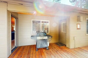 A covered outdoor area with a grill, a door leading to a room, and a window. - Cozy home with private hot tub, patio dining, gas fireplace and full kitchen (Sunriver)