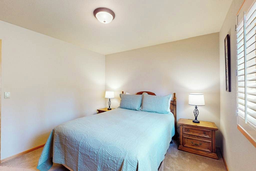 A bedroom with a bed, two bedside tables with lamps, a window with blinds, and a ceiling light.