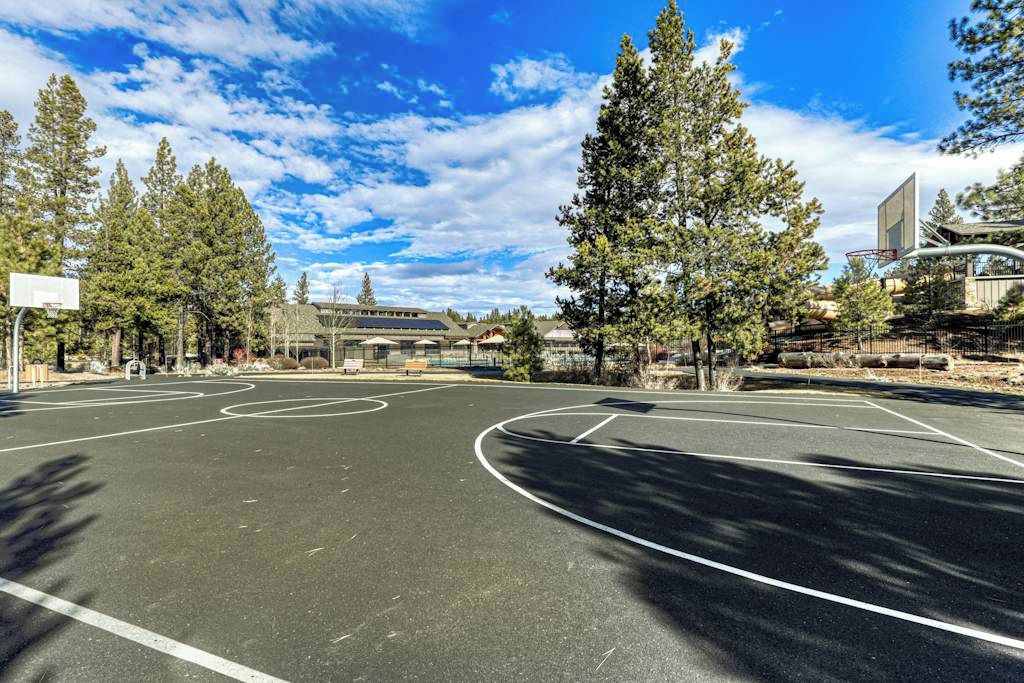 An outdoor basketball court with trees and a building in the background.