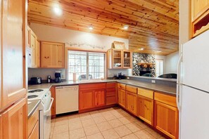 A kitchen with wooden cabinets, a stone wall, and a window. - Cozy home with private hot tub, patio dining, gas fireplace and full kitchen (Sunriver)