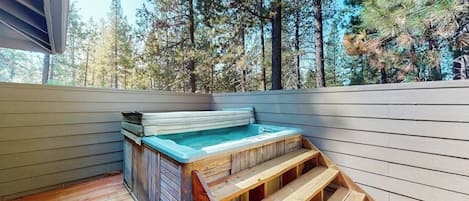 A hot tub on a wooden deck with a view of a forest.