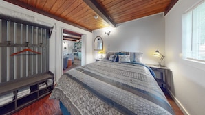 A bedroom with a wooden ceiling, a bed with patterned bedding, a bedside table with a lamp, and a window with blinds. - Dog-friendly home with two full kitchens & a gas grill - walk to the ocean (Reedsport)