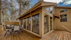 A wooden deck with a table and chairs, large windows, and a view of trees. - Inviting Updated Sunriver Home in Great Location with Large Deck, Private Hot Tub (Sunriver)