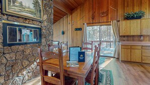 A wooden interior with a stone wall, wooden dining table, chairs, a welcome sign, and a view through a window. - Inviting Updated Sunriver Home in Great Location with Large Deck, Private Hot Tub (Sunriver)