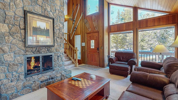 A stone fireplace, leather sofa, and a wooden coffee table in a cozy living room with a staircase and large windows. - Inviting Updated Sunriver Home in Great Location with Large Deck, Private Hot Tub (Sunriver)