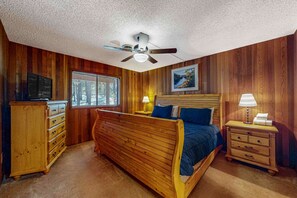 Une chambre à coucher avec un lit en bois, un ventilateur de plafond, une télévision, une fenêtre et une table de chevet avec une lampe.
