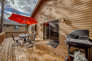 Une terrasse en bois avec une table et des chaises, un barbecue et une porte-fenêtre coulissante.