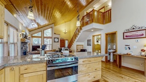 Una cocina amplia con una isla grande, techo de madera y una escalera que lleva a un nivel superior.