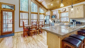 Una cocina amplia con ventanas grandes, piso de madera y una isla central con taburetes.