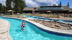 Una piscina con varias pistas, un puesto de socorrista y un edificio con un ventanal grande al fondo.
