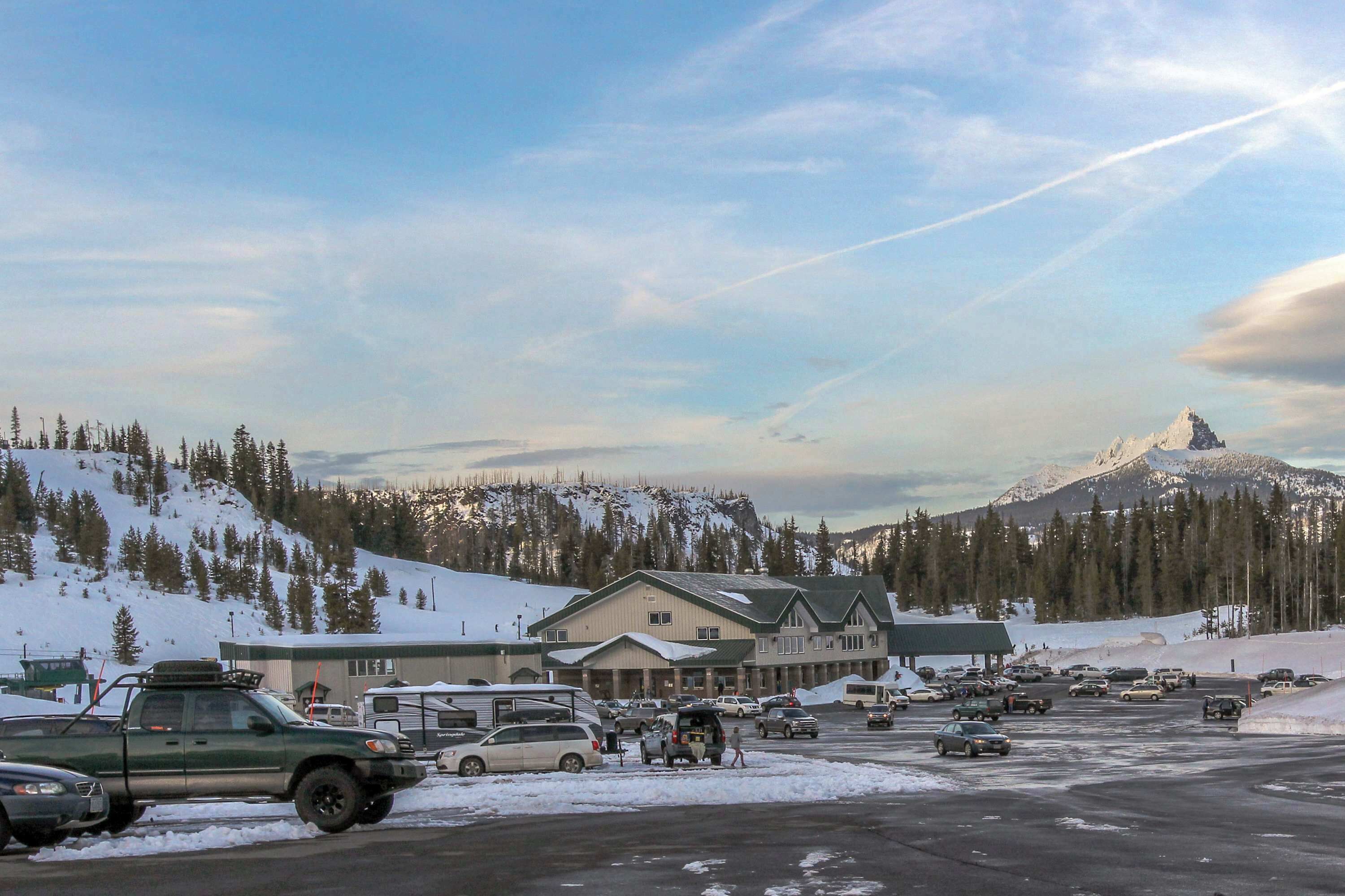 Un parking avec plusieurs véhicules, un bâtiment doté d’un toit végétalisé et, au loin, des montagnes enneigées.