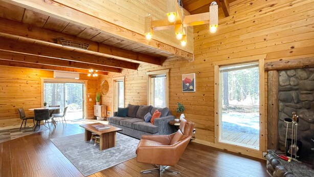 Ein gemütliches Blockhaus-Interieur mit einer Couch, einem Sessel, einem Esstisch und einem Kamin.