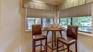 Une pièce d’angle avec deux chaises, une table ronde et une fenêtre avec des stores.
