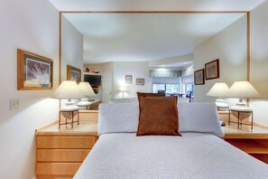 Un dormitorio con una cama grande, lámparas de noche, un aparador de madera y un espejo que refleja la habitación.