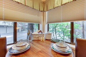 Un comedor con una mesa de madera, dos sillas, una cesta de mimbre, una maceta de cerámica blanca y una ventana con persianas.