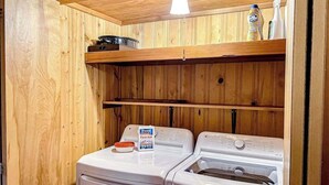 A laundry area with two washing machines, wooden walls, and a shelf with cleaning supplies. - Charming 2-story chalet with deck, wood stove, Deschutes River access (Sunriver)