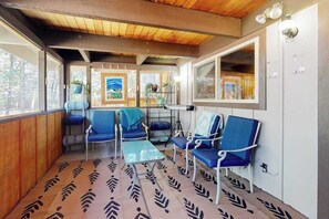 Une cabane avec un plafond en bois, de grandes fenêtres, des chaises bleues, un tapis à motifs et une petite table.