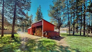 A red barn with a covered area, surrounded by trees and a fenced area. - Charming 2-story chalet with deck, wood stove, Deschutes River access (Sunriver)