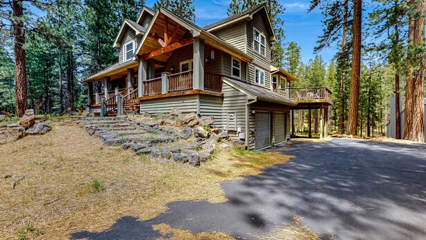 Eine zweistöckige Holzhütte mit Veranda und Garage, umgeben von hohen Kiefern.
