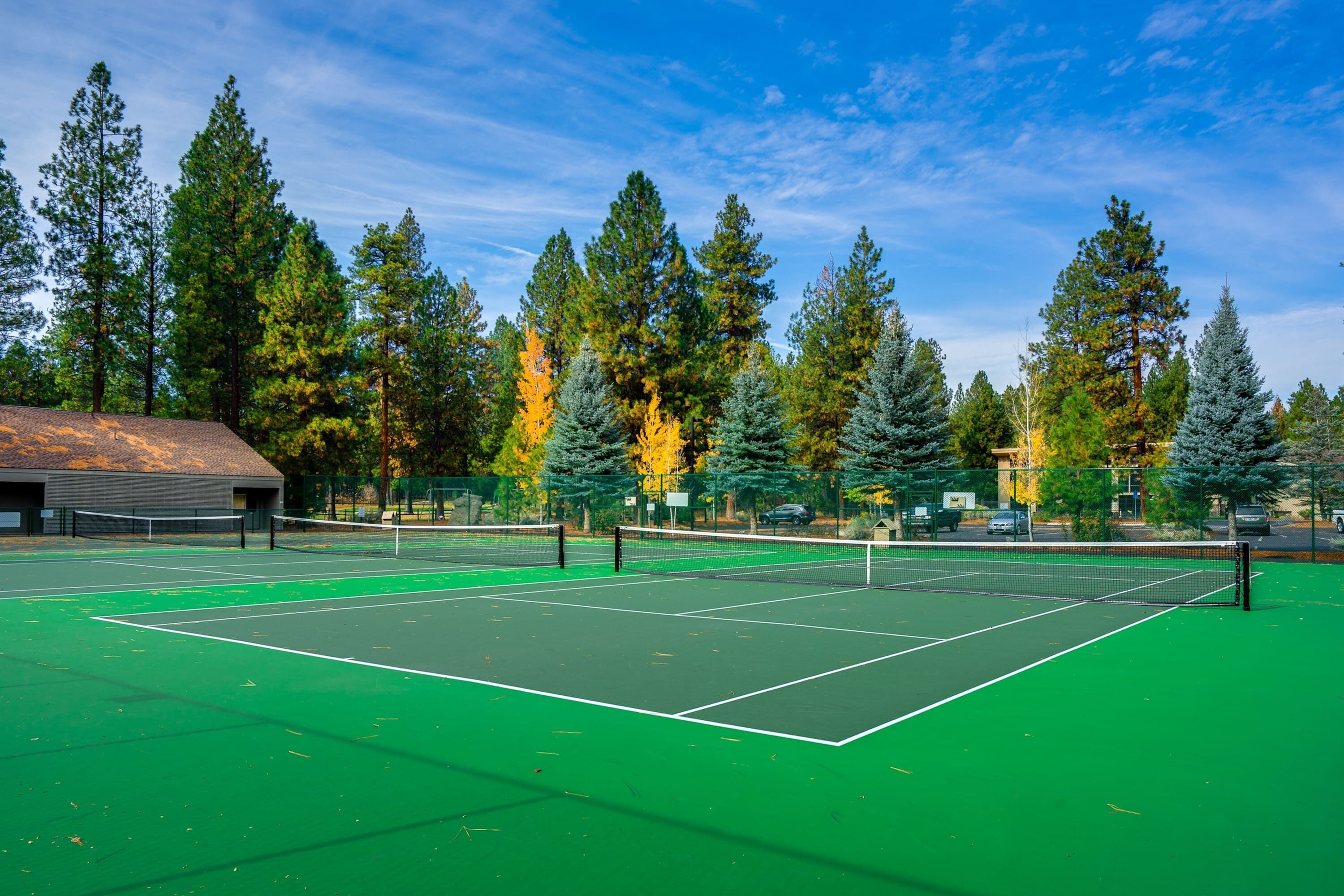 Una cancha de tenis con una red, rodeada de árboles y un edificio.
