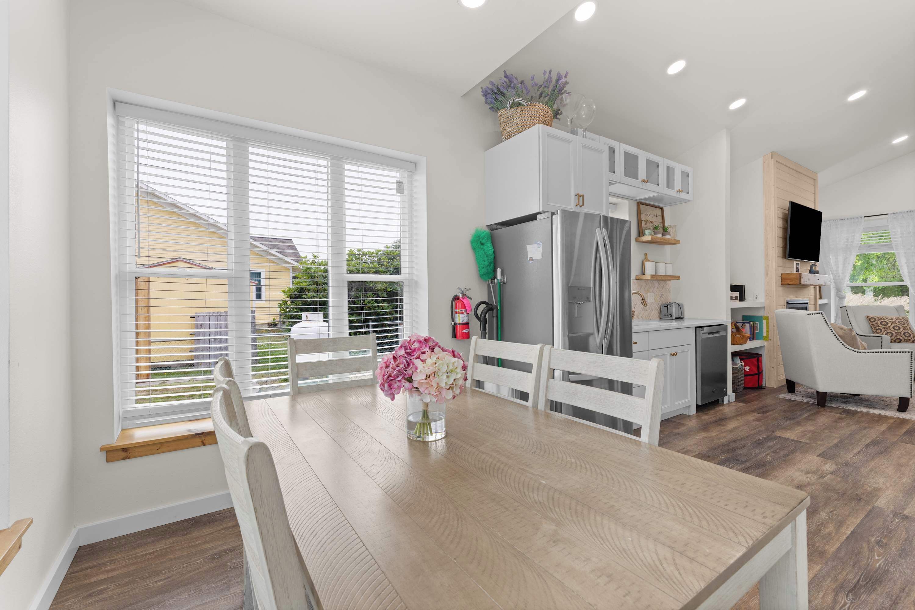 A modern kitchen with white cabinetry, a stainless steel refrigerator, and a dining area with a wooden table and chairs.