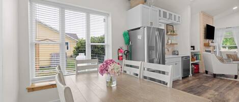 A modern kitchen with white cabinetry, a stainless steel refrigerator, and a dining area with a wooden table and chairs.