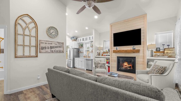 Ein Wohnzimmer mit grauem Sofa, Kamin, Fernseher an einer Holzwand und Deckenventilator.