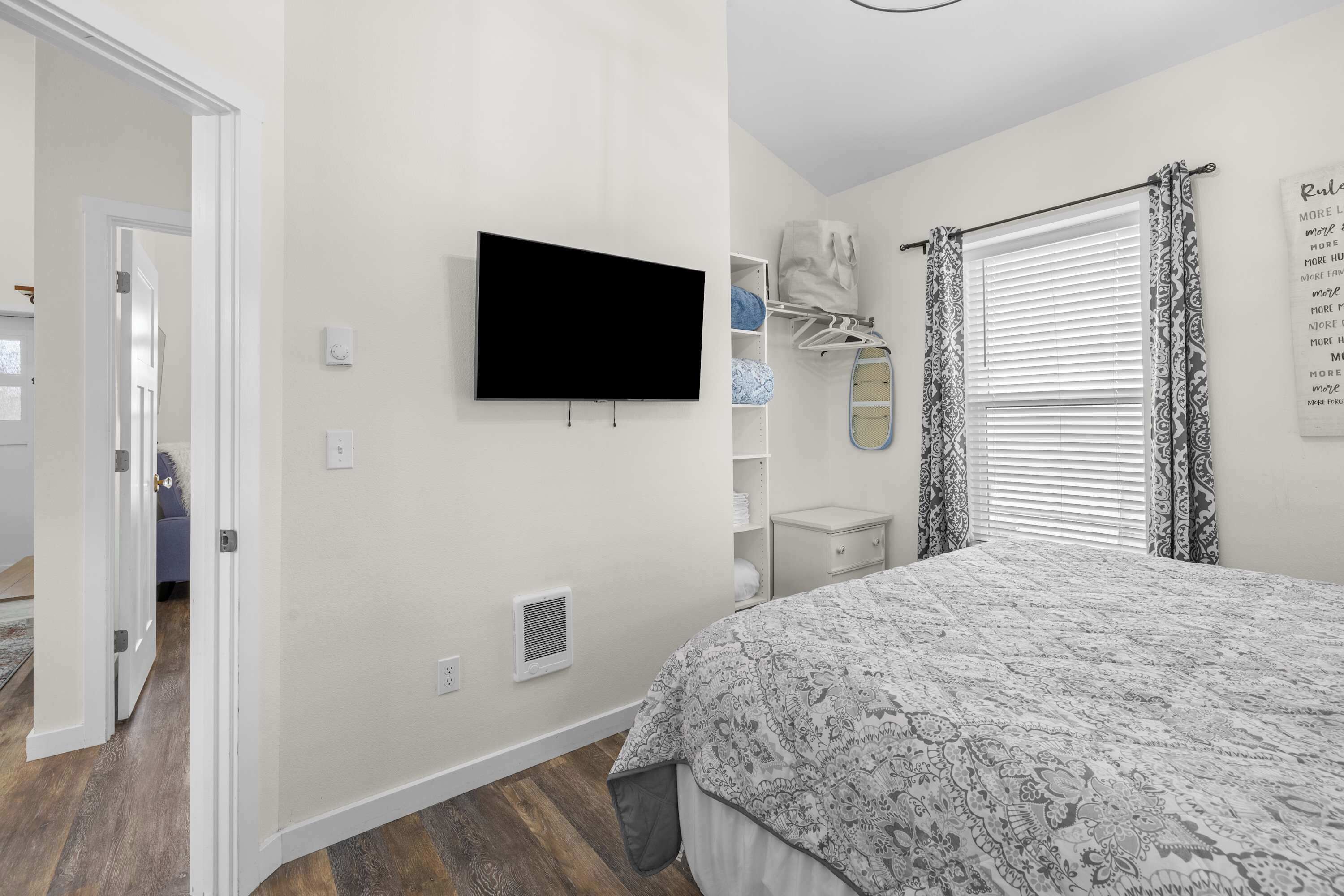A bedroom with a bed, a television, a wardrobe, and a window with patterned curtains.